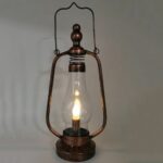Steampunk portable lamp with distressed bronze metal frame and LED candle bulb, front low-angle view on grey studio background