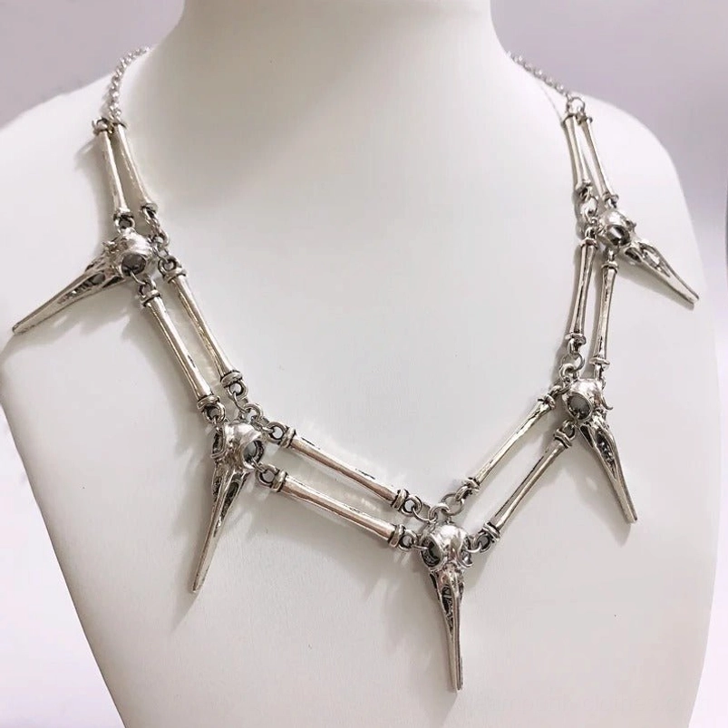 Antique silver bird skull skeleton necklace displayed on mannequin, showcasing polished metal and intricate bone link details