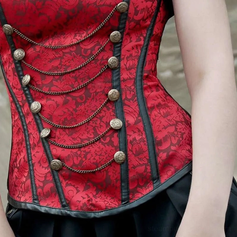 Close-up detail of red jacquard steampunk corset bodice showing antique brass buttons and chain accent