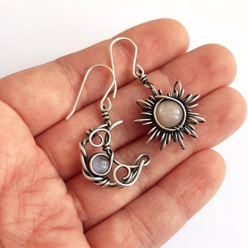 Handcrafted sun and moon drop earrings displayed on palm, showing pink stone on sun charm and iridescent blue stone on moon charm, close-up detail