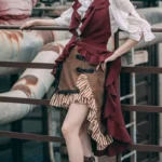 Asymmetrical steampunk skirt with striped ruffle trim and black leather buckles worn by model in outdoor industrial setting