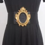 Baroque steampunk corset belt with ornate carved gold oval buckle worn on black dress, front waist view with pure white background