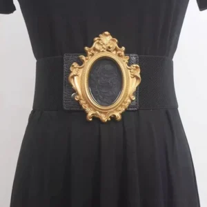 Baroque steampunk corset belt with ornate carved gold oval buckle worn on black dress, front waist view with pure white background
