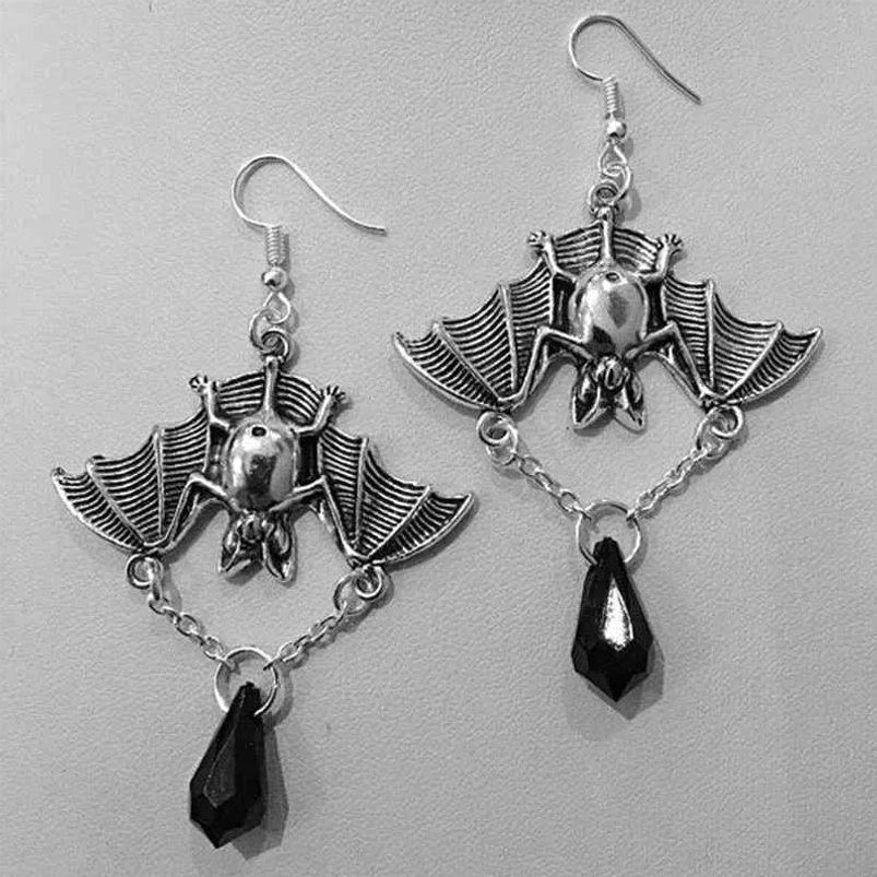 Overhead flat lay of silver metal bat steampunk earrings with black teardrop pendants on light gray studio background, showing full pair design
