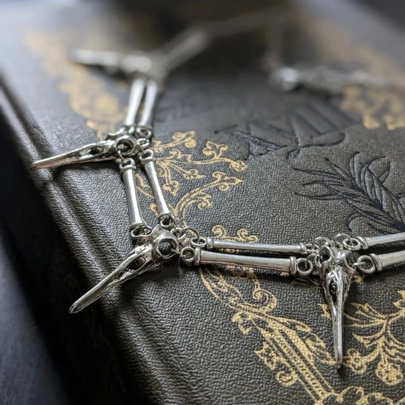 Bird skull skeleton necklace detail shot showing articulated metal joints and silver-toned finish on vintage leather book background