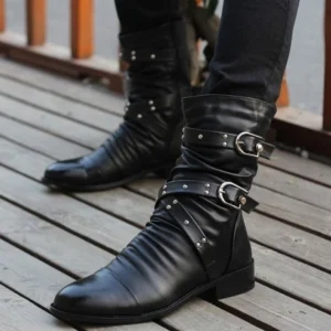 Black steampunk boots with dual buckle straps and ruched shaft, worn by male model on wooden outdoor deck showing pointed toe and studded details