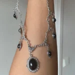 Black gothic steampunk necklace with silver filigree metalwork and black oval gemstone pendant, shown on forearm in side close-up view