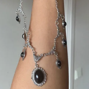 Black gothic steampunk necklace with silver filigree metalwork and black oval gemstone pendant, shown on forearm in side close-up view