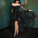 Black off-shoulder high-low steampunk gothic dress with corset bodice and lace flare sleeves, front view on model with dark hair