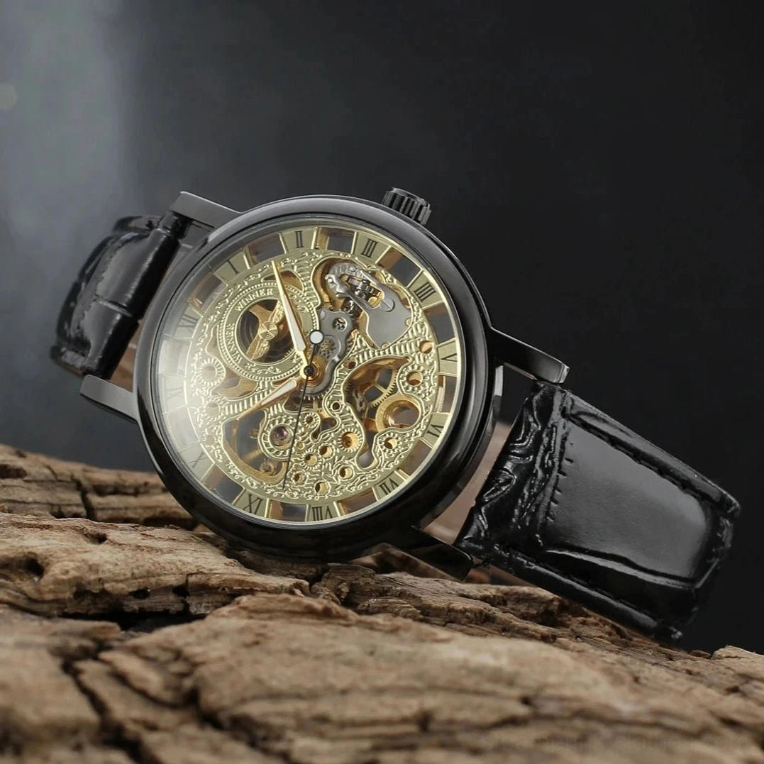 Black steampunk skeleton mechanical watch with gold hollow movement and Roman numeral dial, displayed on dark wooden surface with oblique top-down view showcasing leather strap detail