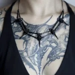 Black steampunk bird skull necklace with articulated metal skeleton design, worn by tattooed model for gothic alternative fashion styling