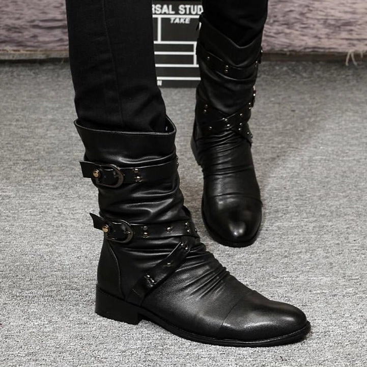 Black steampunk boots worn by male model featuring polished leather, multiple buckle straps, and pointed toe silhouette against film studio backdrop