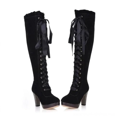 Black suede steampunk over-the-knee boots with high block heel and satin ribbon laces, flat front view on white background