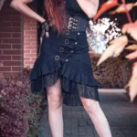 Black steampunk mermaid skirt with multiple front buckles, asymmetrical ruffled lace hem, worn by red-haired model in outdoor garden setting