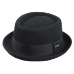 Black steampunk fedora hat with gold metal badge detail, shown from left three-quarter angle on plain background