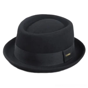 Black steampunk fedora hat with gold metal badge detail, shown from left three-quarter angle on plain background