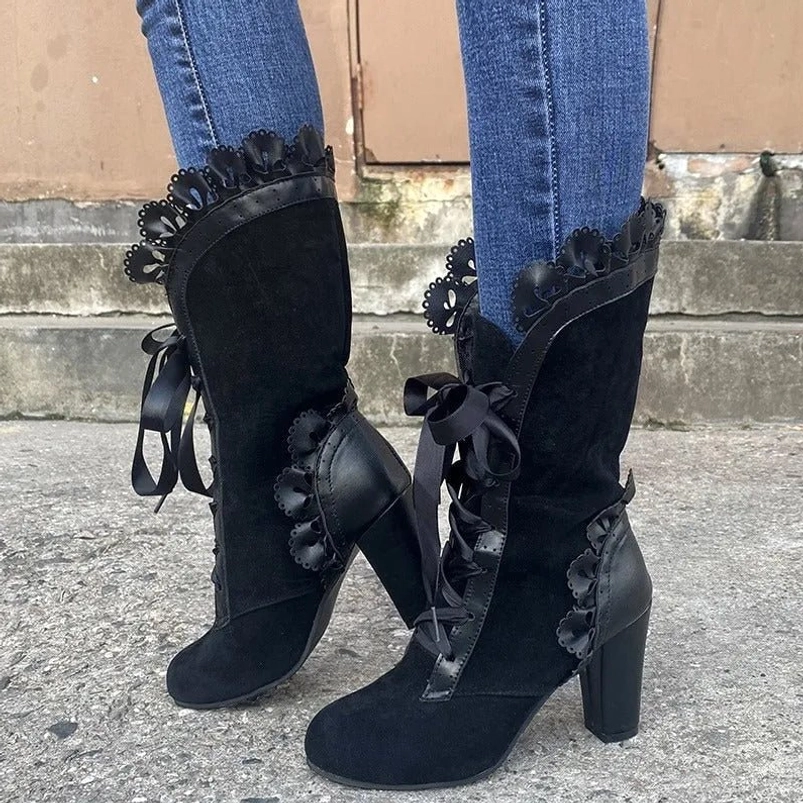 Black steampunk lace-up boots with bow ribbon details and block heel, front three-quarter view on outdoor concrete pavement
