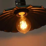 Black steampunk industrial pendant lamp with fluted metal shade and warm Edison bulb, low-angle bottom view showcasing ribbed design and bronze lamp socket