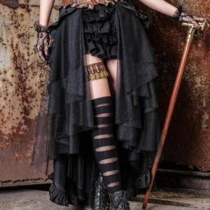Black steampunk high-low overlay skirt with sheer tulle front and ruffled hem, styled with striped stockings and lace gloves on rusty industrial wall backdrop