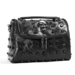 Black leather steampunk skull handbag front three-quarter view featuring prominent silver skull hardware, decorative round rivets, and intricate patchwork leather segments with precision black stitching