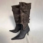 Black steampunk mid-calf stiletto boots front three-quarter view, distressed leather with frayed canvas cuffs, metal buckles and chains detail