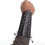 Black studded leather wrist armor with round and teardrop metal rivets worn on male mannequin hand, frontal side view showing stud detail and lace-up fastening system