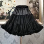 Black tiered tulle steampunk skirt front view with adjustable elastic waist, displayed on dress mannequin with voluminous layered ruffled hem details against vintage decorative backdrop