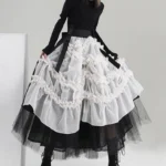 Black and white steampunk ruffled skirt with sheer organza overlay and black tulle underskirt, shown on lower body model from left three-quarter angle, displaying layered ruched frills and mid-calf length