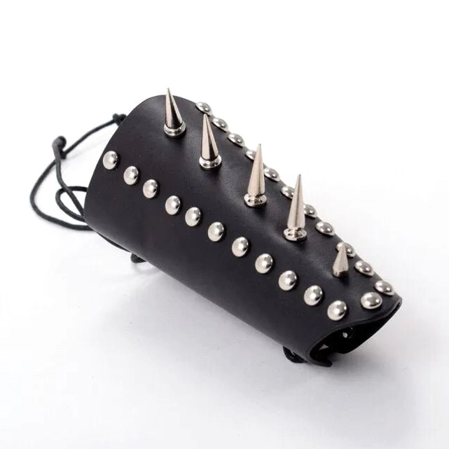 Spike studded black leather wrist armor with adjustable lace-up fastener and mixed stud heights, angled side flat lay photograph