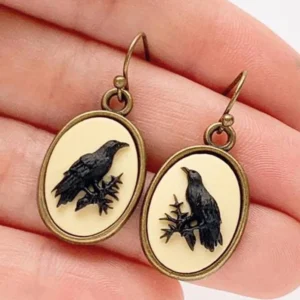Antiqued bronze raven cameo drop earrings with black raven relief on cream base, held in hand showing close-up detail and hanging length