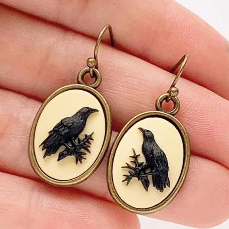 Antiqued bronze raven cameo drop earrings with black raven relief on cream base, held in hand showing close-up detail and hanging length