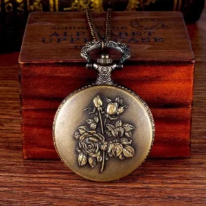 Vintage steampunk pocket watch with embossed rose pattern, bronze metal finish, front view on wooden desktop with retro wooden box, ornate top hook and hardware detail