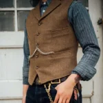 Vintage steampunk brown herringbone tweed waistcoat with silver waist chain and flap pockets, worn outdoors near white wooden door