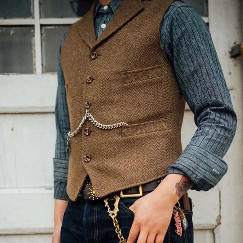 Vintage steampunk brown herringbone tweed waistcoat with silver waist chain and flap pockets, worn outdoors near white wooden door