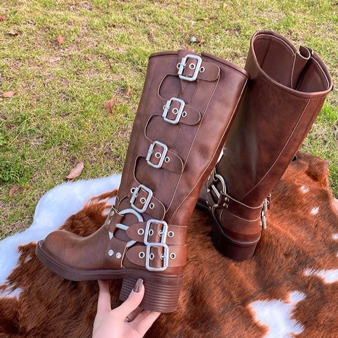 Brown steampunk boots with multiple layered silver buckles and chunky block heel, held in hand on outdoor rug