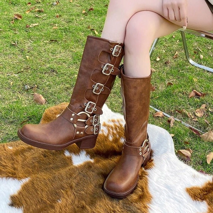 Brown steampunk calf boots with chunky heel and layered silver hardware buckles, three-quarter seated view on outdoor rug