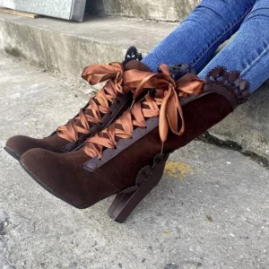 Brown steampunk lace-up boots with satin ribbon ties and scalloped collar trim, mid-calf height, worn with blue jeans on outdoor concrete steps
