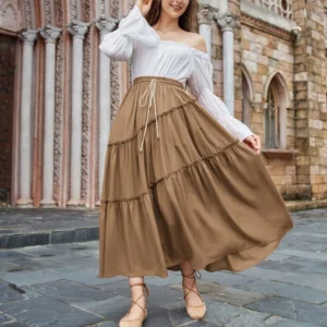 Brown tiered maxi skirt with ruffled layers worn by model in Victorian stone church courtyard, front three-quarter view showing elastic drawstring waist and cascading ruffled silhouette