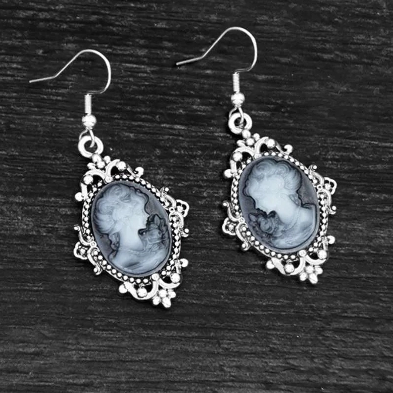 Steampunk cameo drop earrings flat lay on dark wooden surface showing ornate silver border and grey-white marbled cameo detail