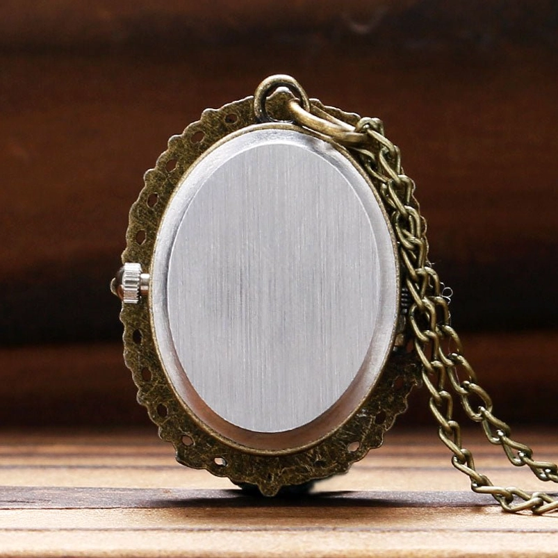 Back side of ornate cameo pocket watch pendant in close-up, displaying brushed silver metal surface and detailed bronze filigree frame on wooden tabletop