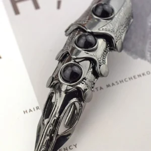 Full finger joint armor ring close-up showing articulated segmented metal joints, black gem inlays, and textured gunblack metallic finish