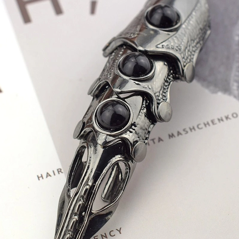 Full finger joint armor ring close-up showing articulated segmented metal joints, black gem inlays, and textured gunblack metallic finish