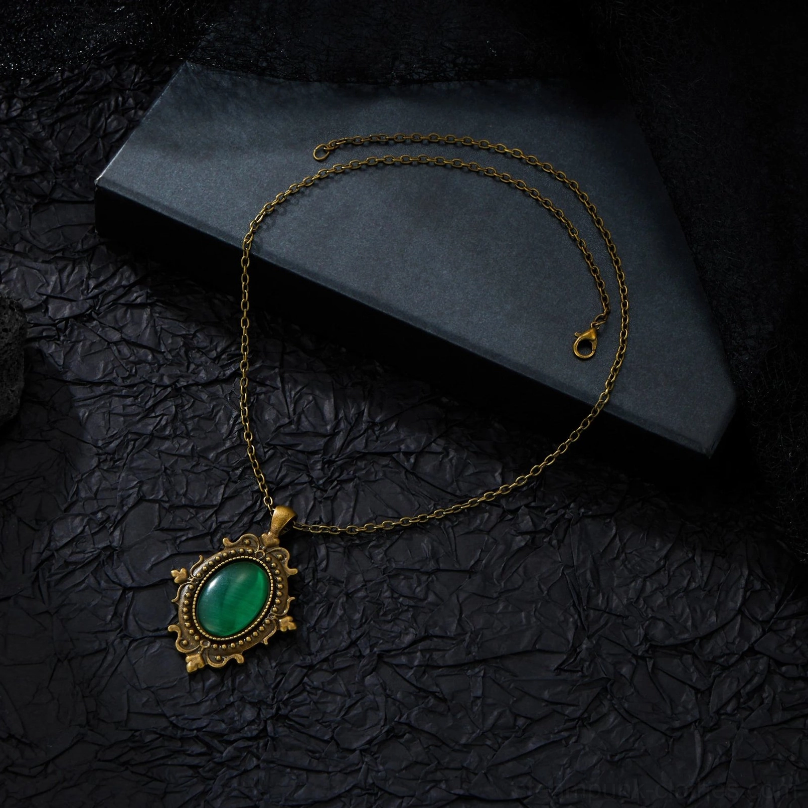 Full steampunk Victorian green necklace with scrollwork metal frame and emerald cat-eye stone displayed on black crinkled background