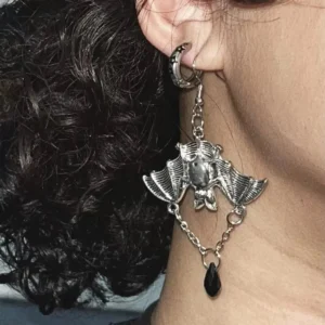 Close-up side view of single silver bat steampunk earring worn on earlobe, showing intricate engraved bat charm and hoop ear hook detail