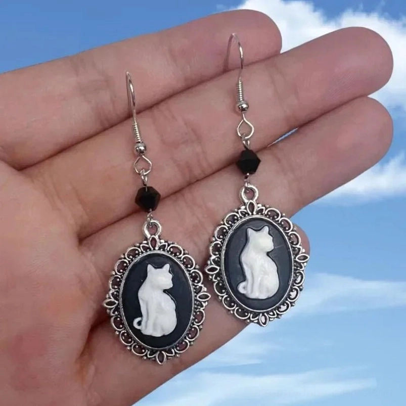 vintage cat cameo earrings worn on hand showing black faceted bead and silver ear wire detail against sky backdrop