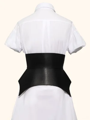 Steampunk bat corset belt rear view on mannequin wearing white shirt dress, showcasing asymmetric black faux leather hem and tapered back silhouette