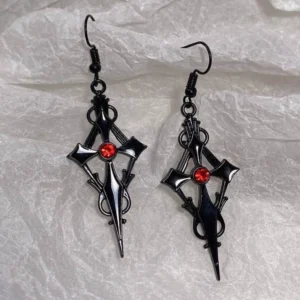 Flat lay overhead view of black gothic cross dangle earrings with ornate filigree and red rhinestone accent on fabric backdrop