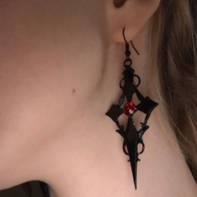 Gothic cross drop earrings worn on female ear showing black metal and red crystal center, steampunk jewelry on model