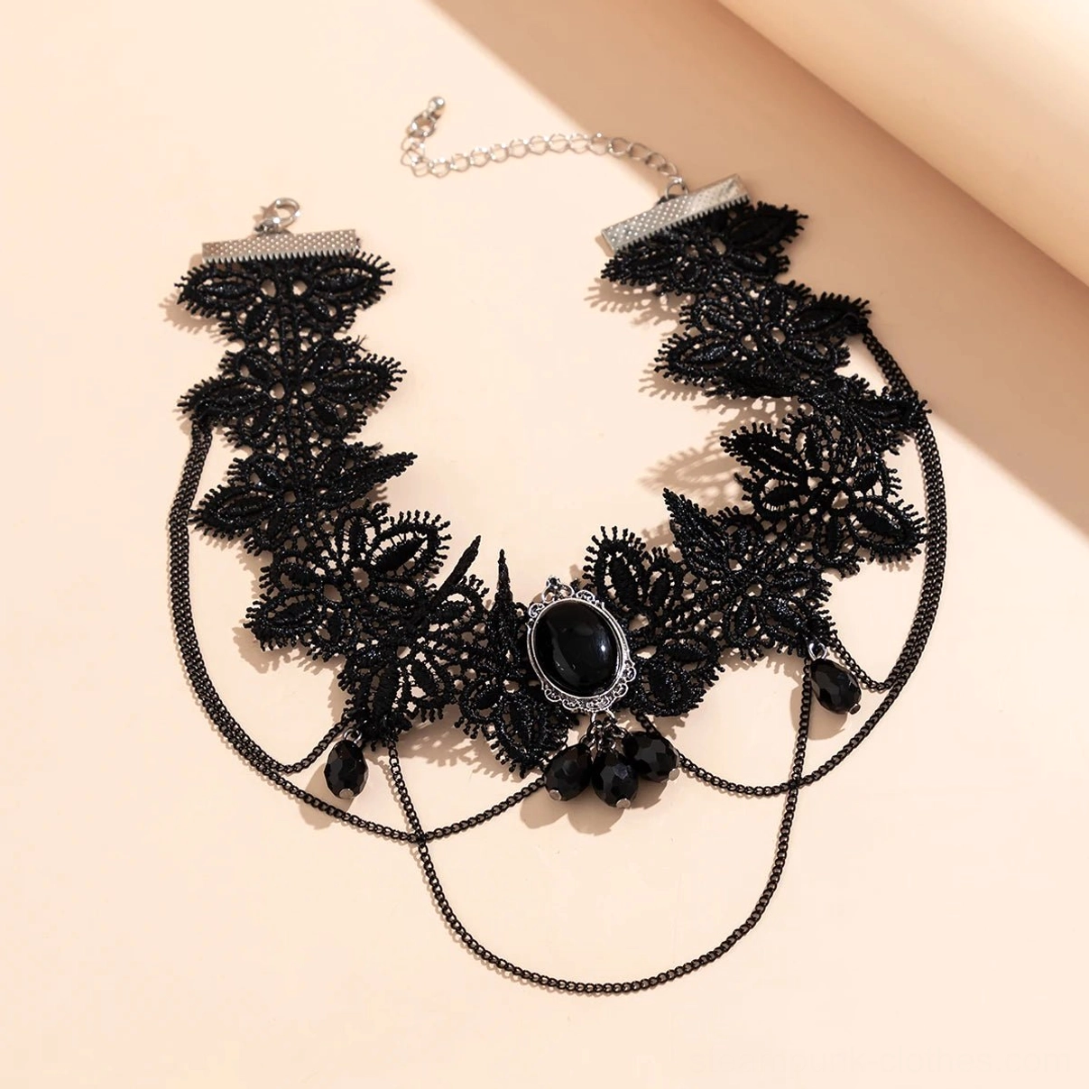 Flat lay product shot of black lace choker showing full length, central black gem, adjustable chain clasp system, and teardrop pendant accents on neutral background