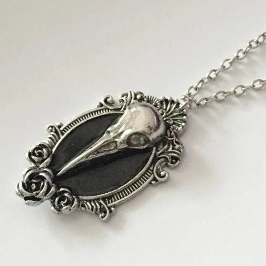 Side oblique view of gothic bird skull steampunk necklace showing rose-shaped scroll decorations, vintage silver tone finish, and black enamel inlay detail